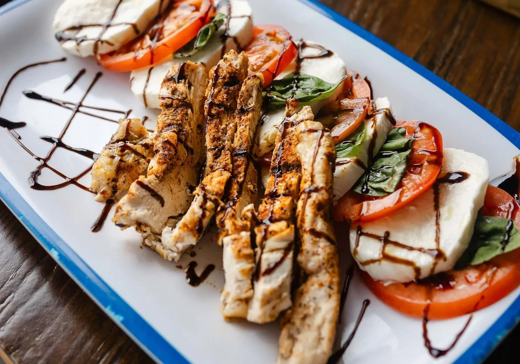 Plated grilled chicken and Caprese salad with balsamic glaze.