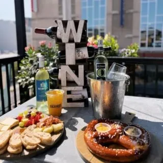 Appetizer board, soft pretzel, and wine on an outdoor patio table.