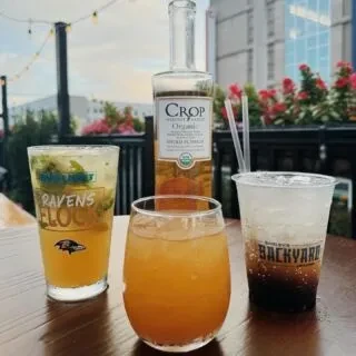 Three varied drinks and a vodka bottle on an outdoor table.