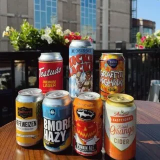 Seven unique branded canned beers and ciders on an outdoor table.