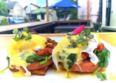 Two plates of Eggs Benedict with spinach, tomato, and hollandaise outdoors.