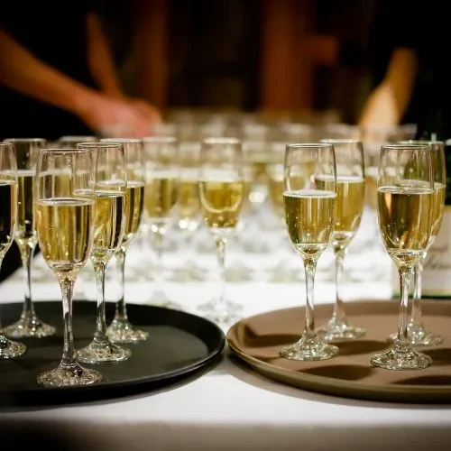 Numerous golden champagne flutes arranged on serving trays at an event.