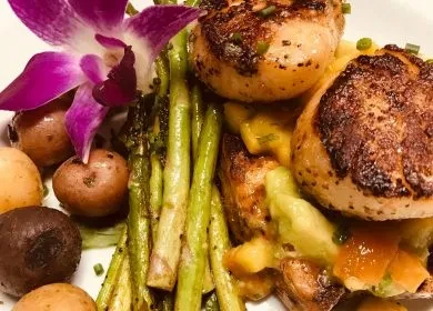 Seared scallops, asparagus, colorful potatoes, and an orchid on a white plate.