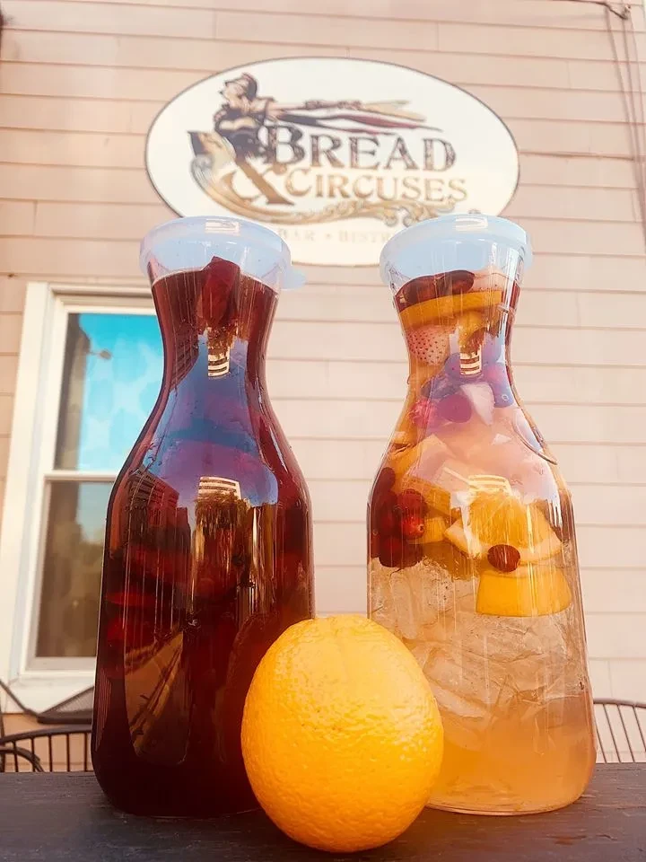 Two pitchers of sangria and fruit water on an outdoor table.