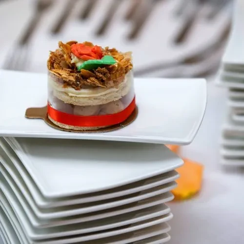 Cylindrical layered pastry with a red rose on a white plate.