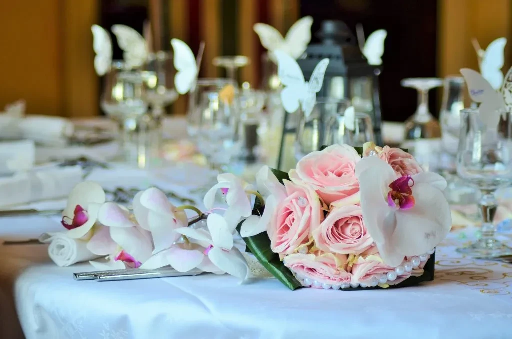 Elegant table centerpiece with pink roses, white orchids, butterfly glasses.
