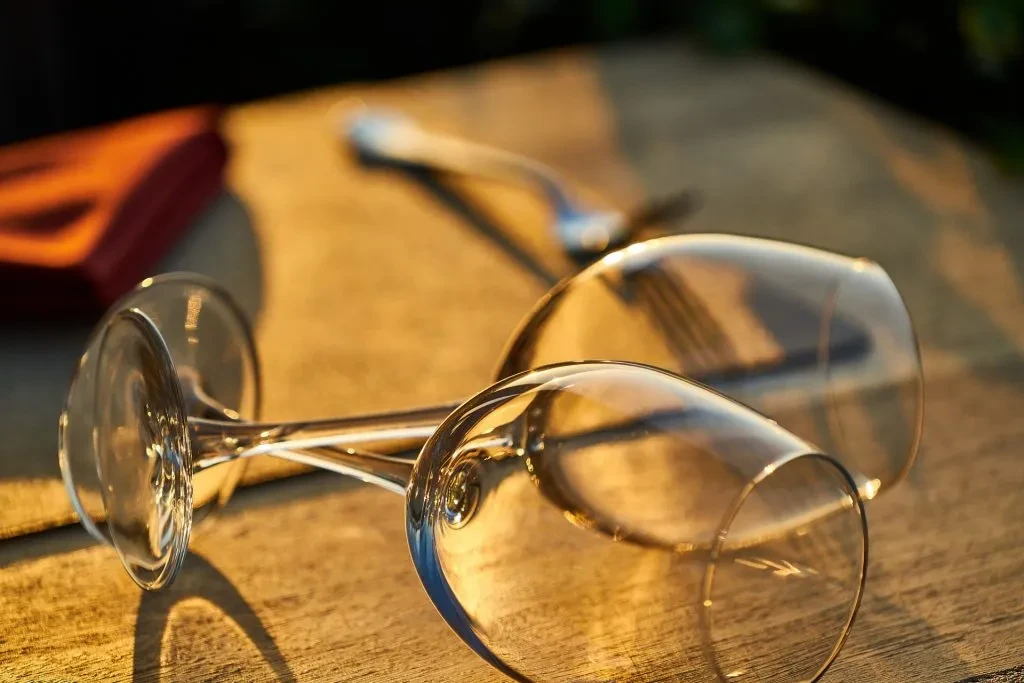 Two empty wine glasses lie on a rustic wooden surface in golden light.