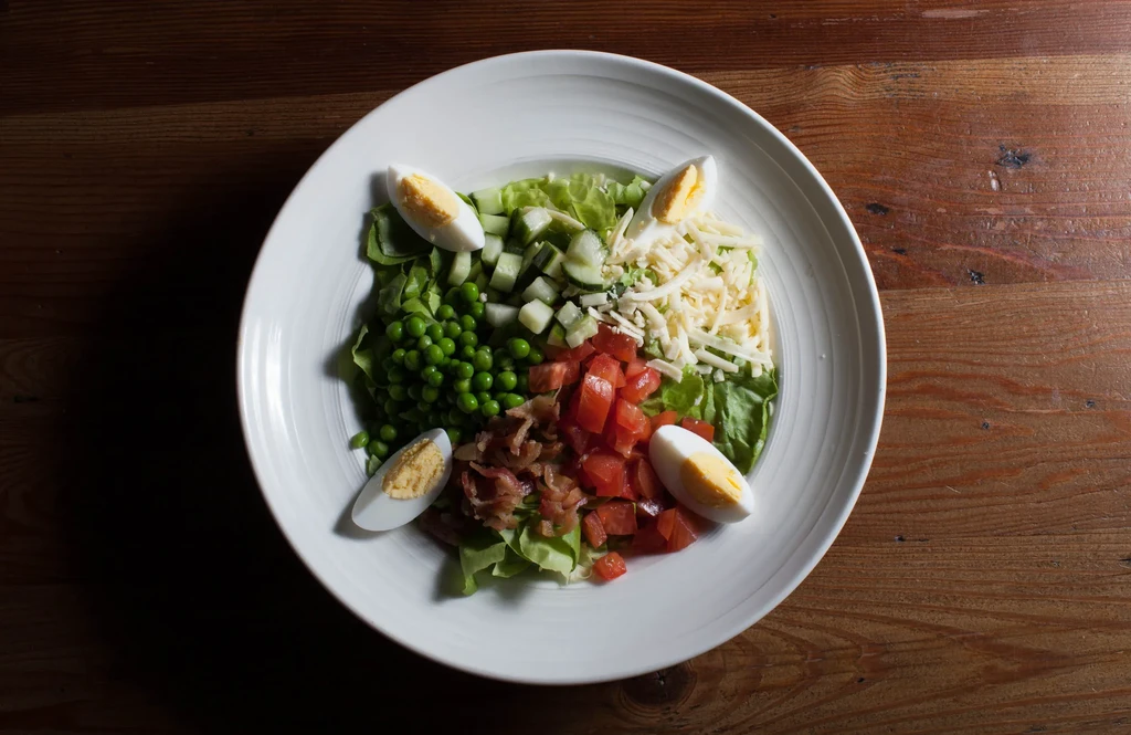 Vibrant sectional salad with eggs, bacon, vegetables on rustic wooden table.