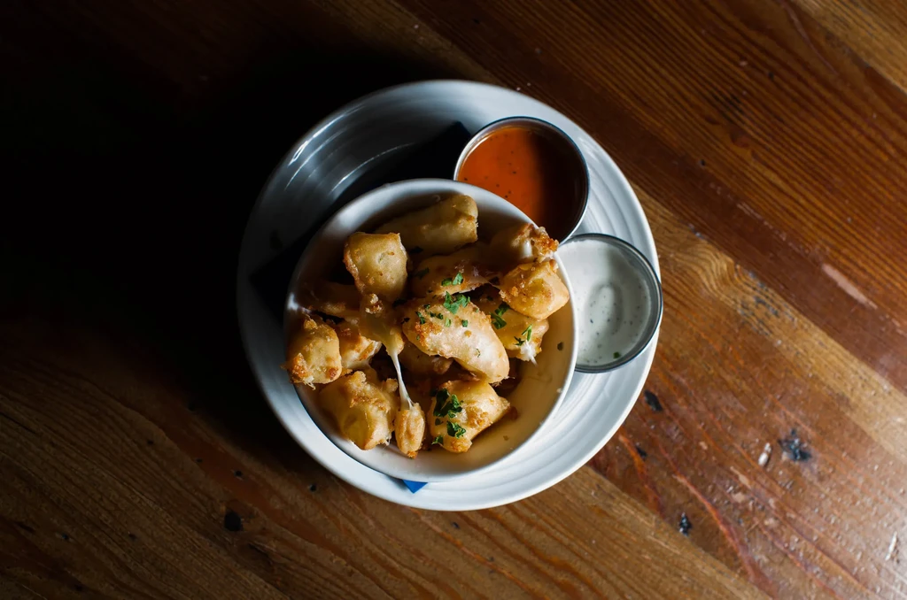 Golden-brown fried cheese curds with herbs, marinara, and a creamy dip.