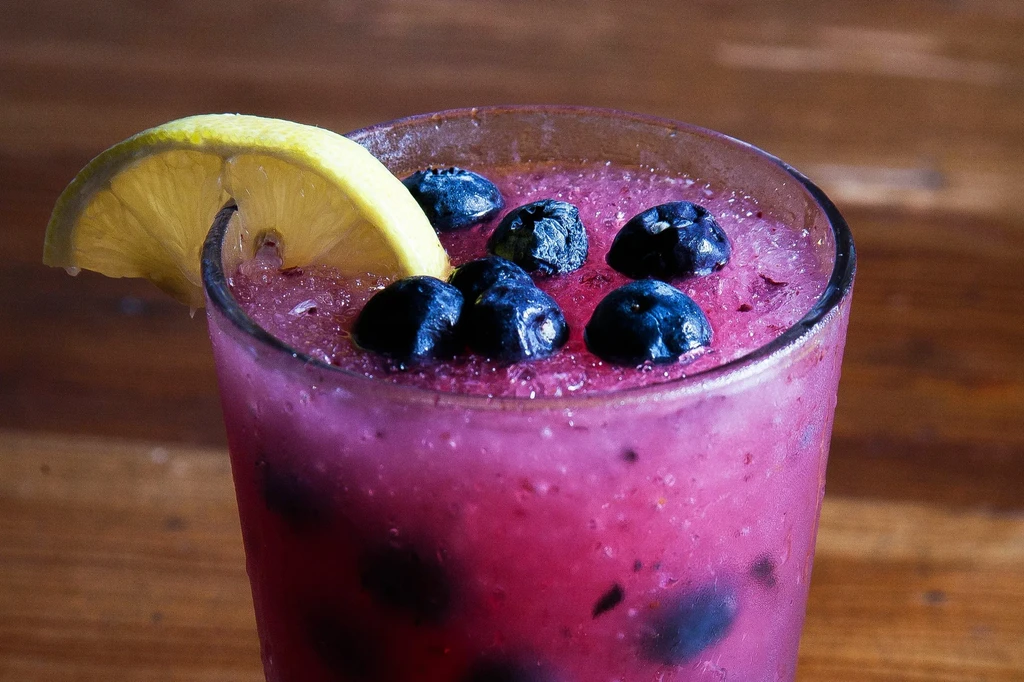 Icy magenta drink in a clear glass with blueberries and lemon.