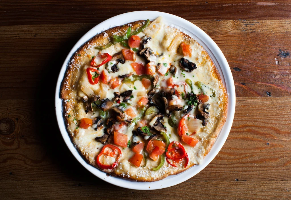 Top-down pizza with melted cheese, tomatoes, mushrooms, peppers, onions, herbs.