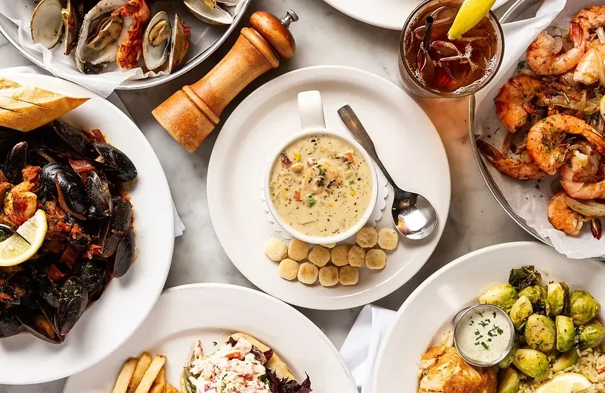 Flat lay of multiple plates of various seafood and drinks.