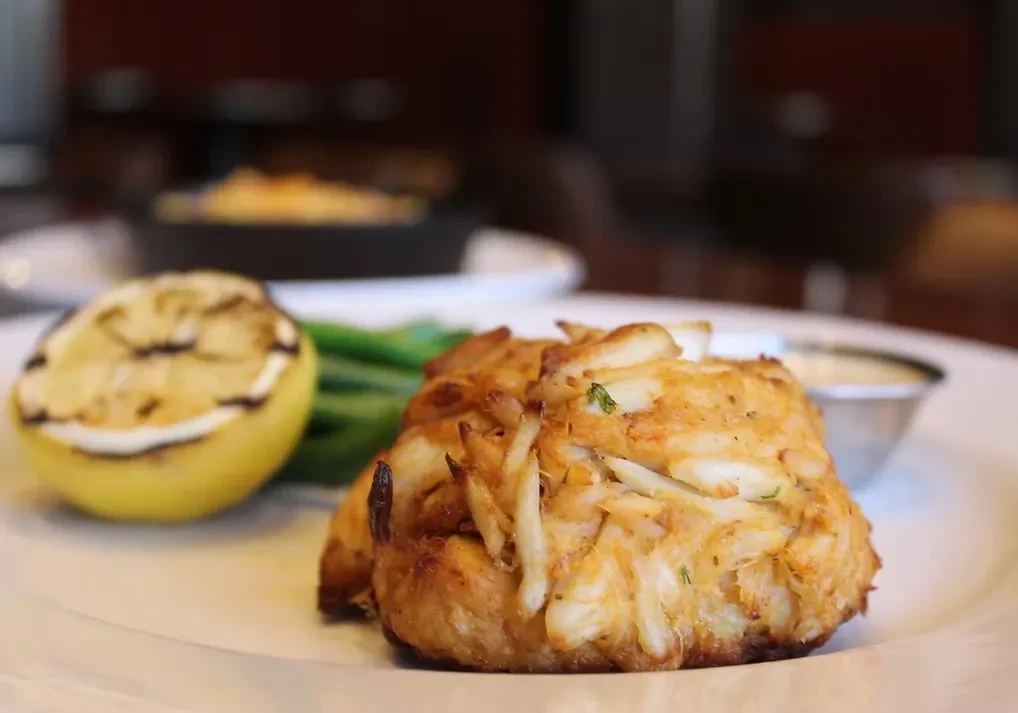 Golden-brown crab cake, grilled lemon, green beans, and white sauce.