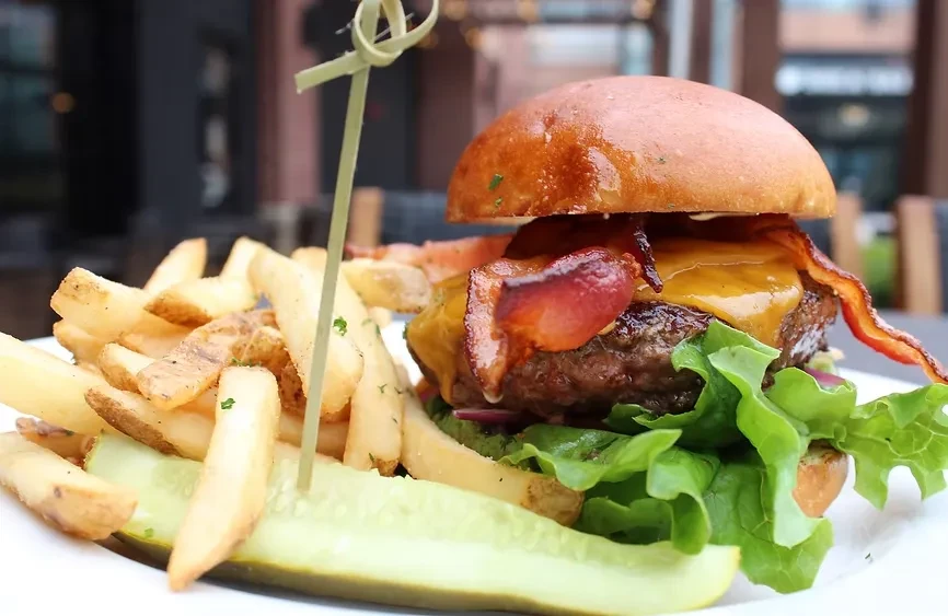 Gourmet burger with bacon, cheese, fries, pickle spear.