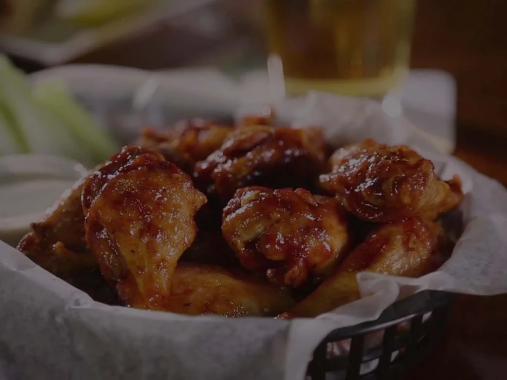 Sticky, sauced chicken wings in a basket with dip and celery sticks.