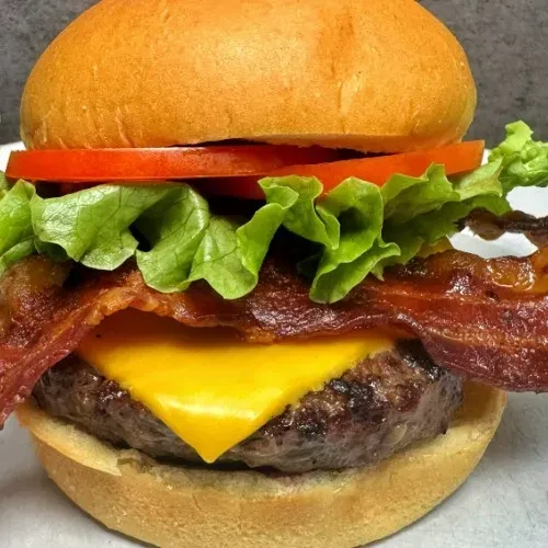 Layered bacon cheeseburger with crispy bacon, melted cheese, lettuce, and tomato.