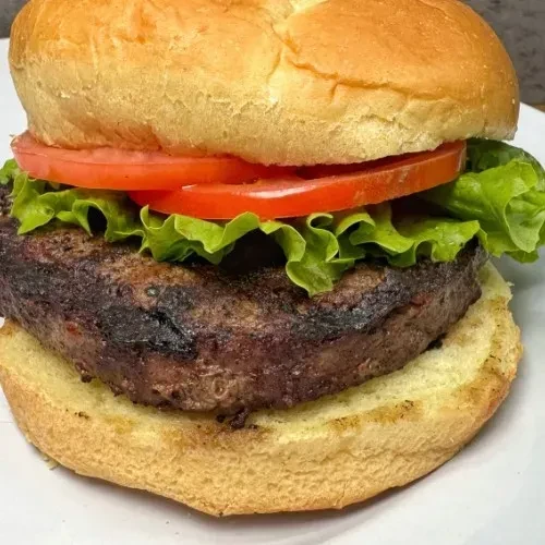 Close-up: Hamburger with grilled patty, lettuce, tomato on white plate.