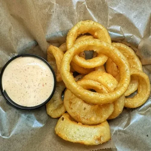 Golden-brown onion rings with creamy dipping sauce in a lined basket.