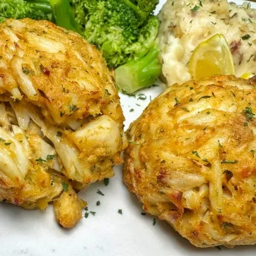 Golden-brown crab cakes, broccoli, mashed potatoes, and lemon wedge.