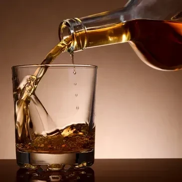 Amber liquid pours from bottle into glass, splashing.