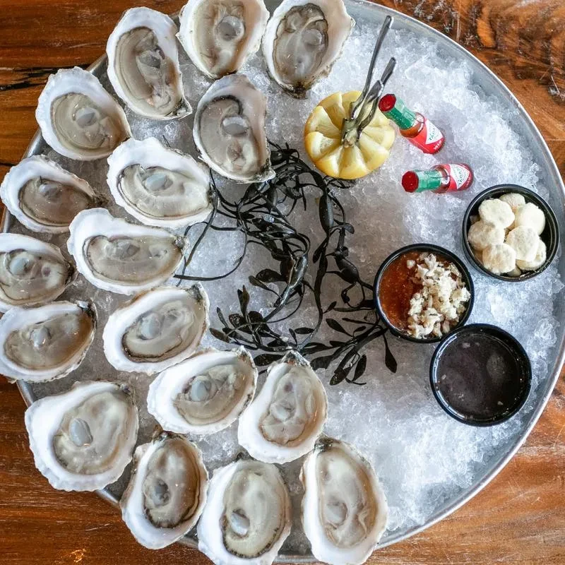 A platter of 20 freshly shucked oysters on ice with condiments.