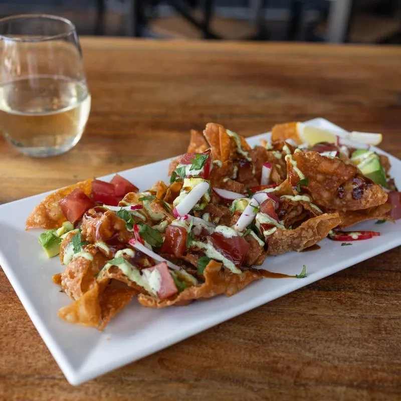 Deconstructed tuna poke nachos with wontons, avocado, radish, and two sauces.