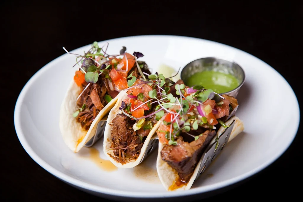 Three gourmet tacos with shredded meat, pico de gallo, microgreens, green sauce.