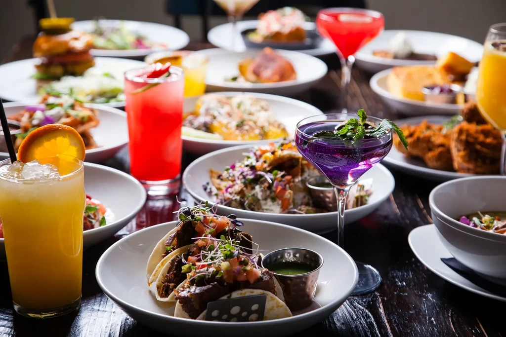 Tacos, various cocktails, and other food on a wooden table.