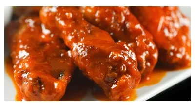 Several chicken wings coated in glossy orange-red sauce.