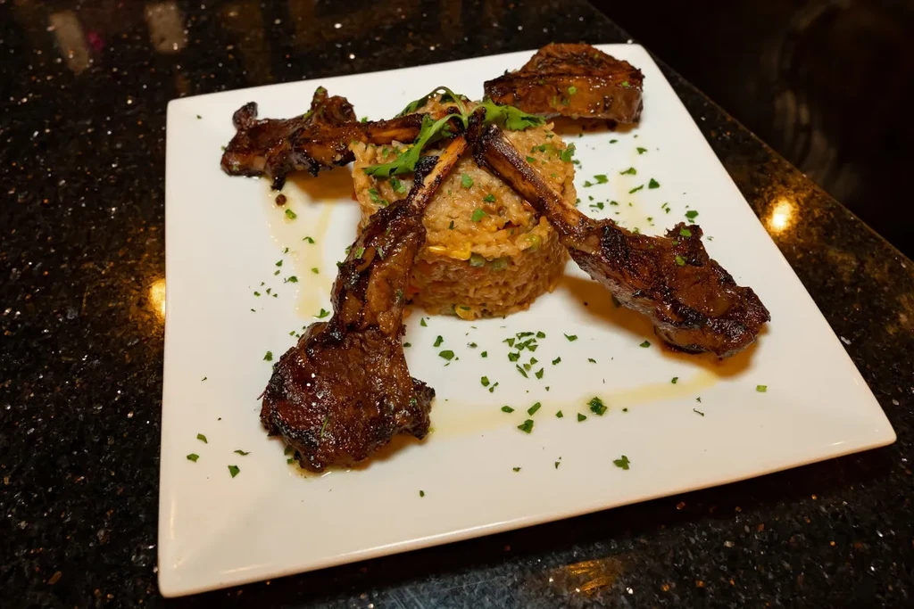 Five gourmet lamb chops and rice pilaf on a white plate.