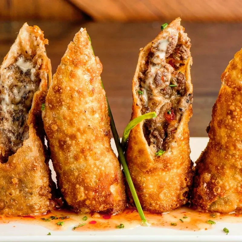 Four crispy fried rolls with meat and cheese filling, sauce, and herbs.