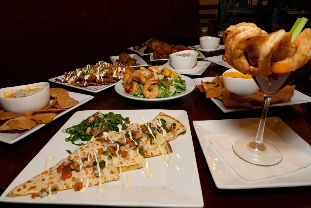 Restaurant table laden with quesadillas, nachos, salads, and a shrimp cocktail.