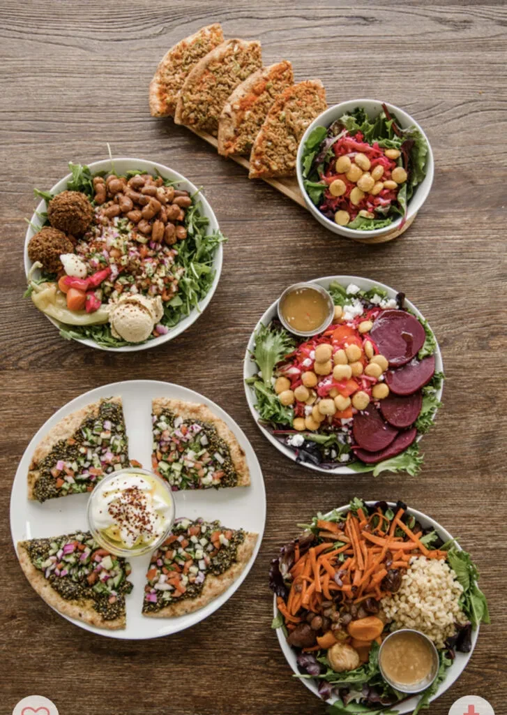 Overhead of diverse salads and flatbreads on a rustic wooden table.