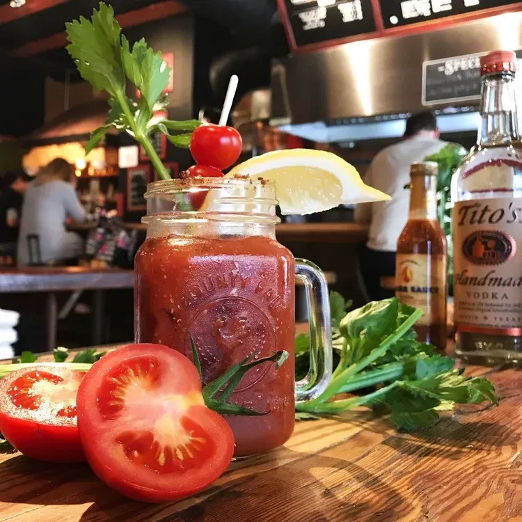 Garnished Bloody Mary cocktail in mason jar on rustic wood table.