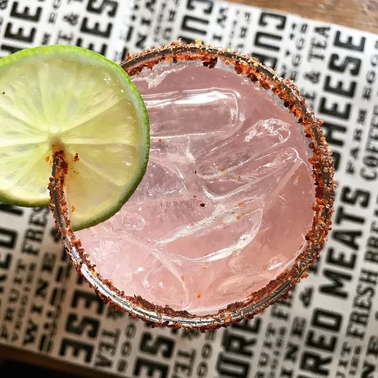 Pink iced drink with chili-lime rim and lime slice on placemat.