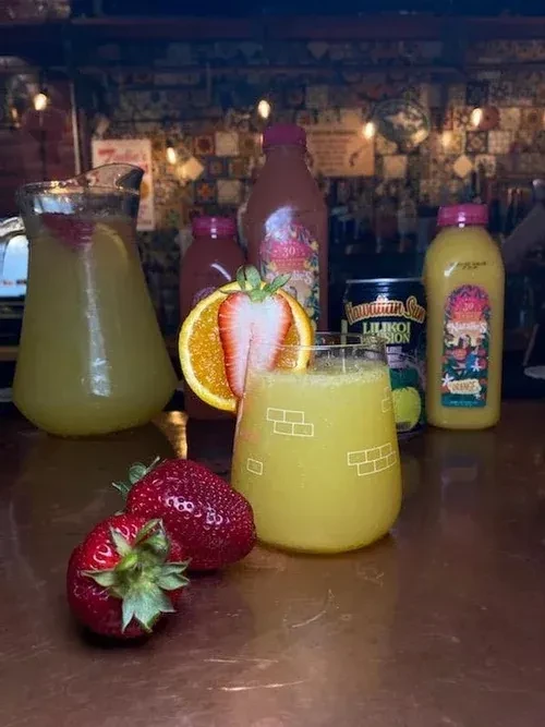 Fresh strawberries, yellow drinks, and bottles on a reflective bar.