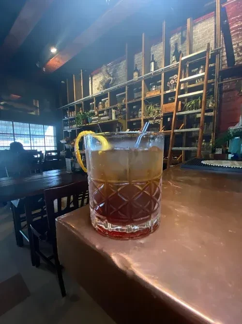 Old-fashioned cocktail in ornate glass with lemon peel on bar.