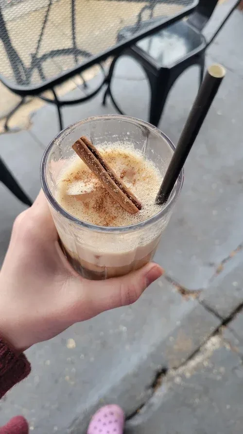 Iced latte with cinnamon sticks, held by a hand at an outdoor cafe.