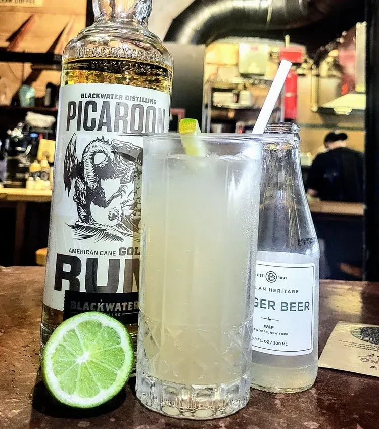Rum bottle, cocktail with lime, ginger beer, and lime on bar.