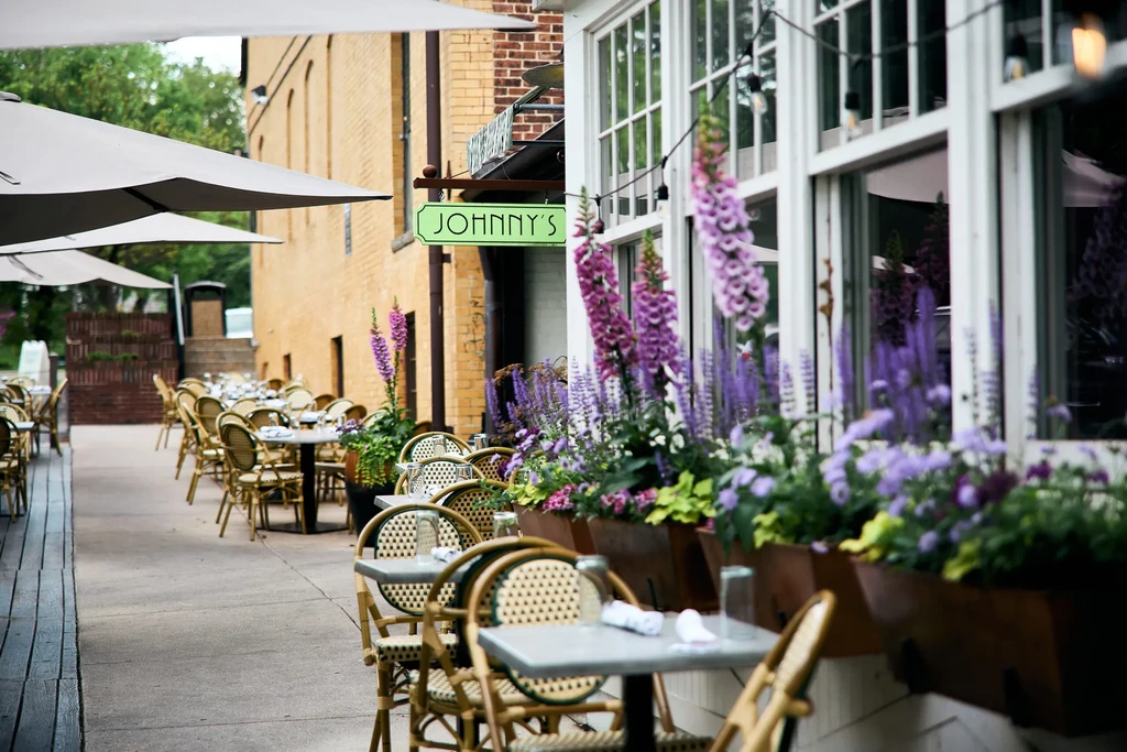 Restaurant patio with set tables, wicker chairs, umbrellas, and purple flowers.