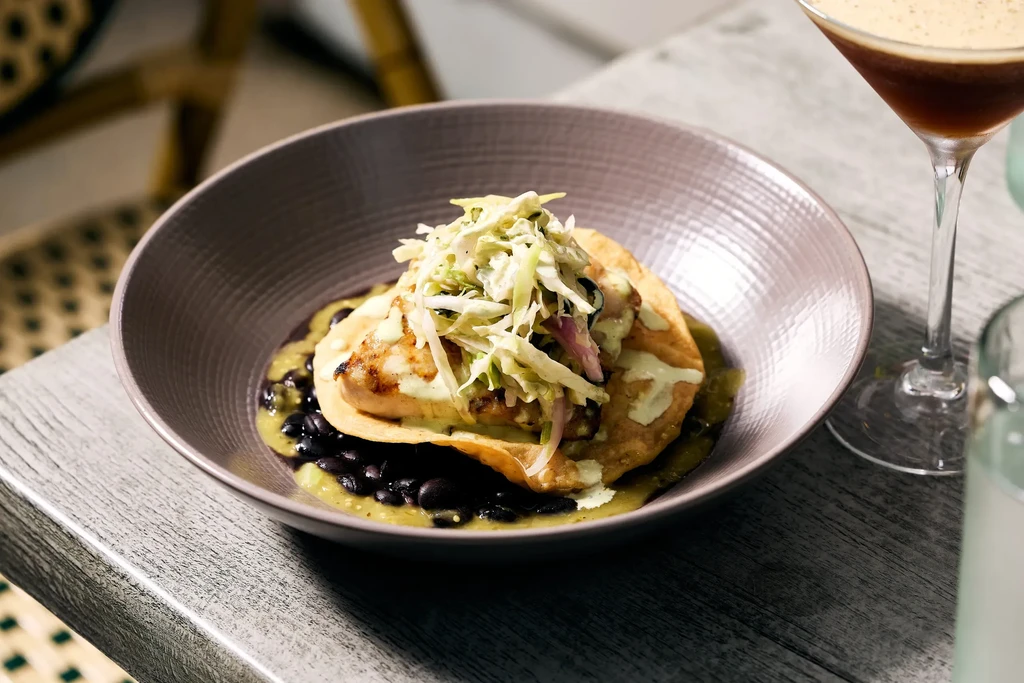 Tostada with grilled protein, cabbage slaw, black beans, and green sauce.