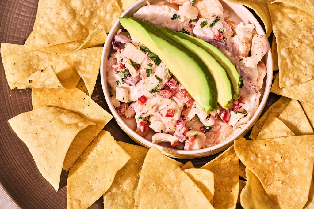 Close-up of a bowl of seafood salad with avocado and tortilla chips.