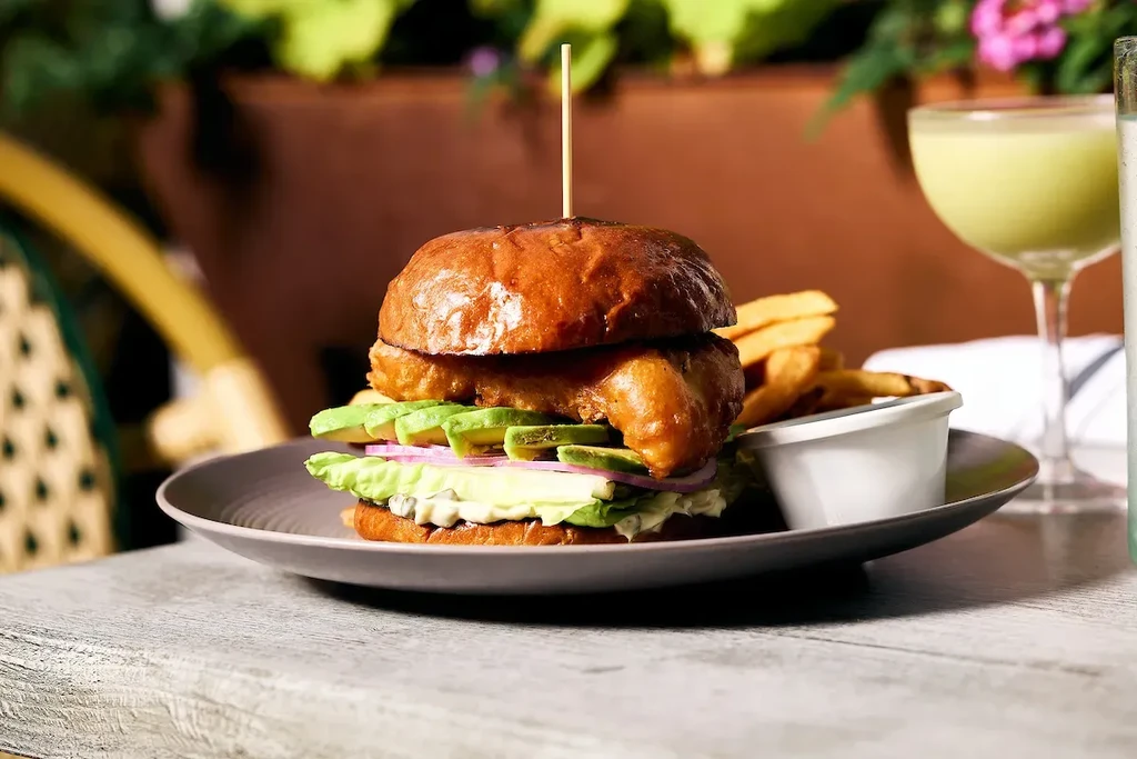 Breaded fish burger with fries and a drink served outdoors.