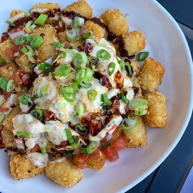 Golden tater tots with creamy and dark sauces, scallions, and diced tomatoes.
