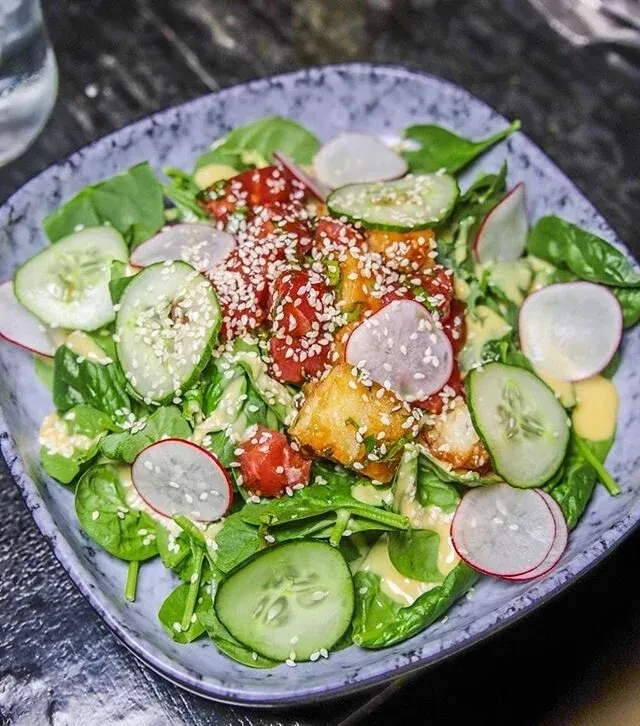 A vibrant spinach salad with golden tofu, radish, cucumber, and sesame seeds.