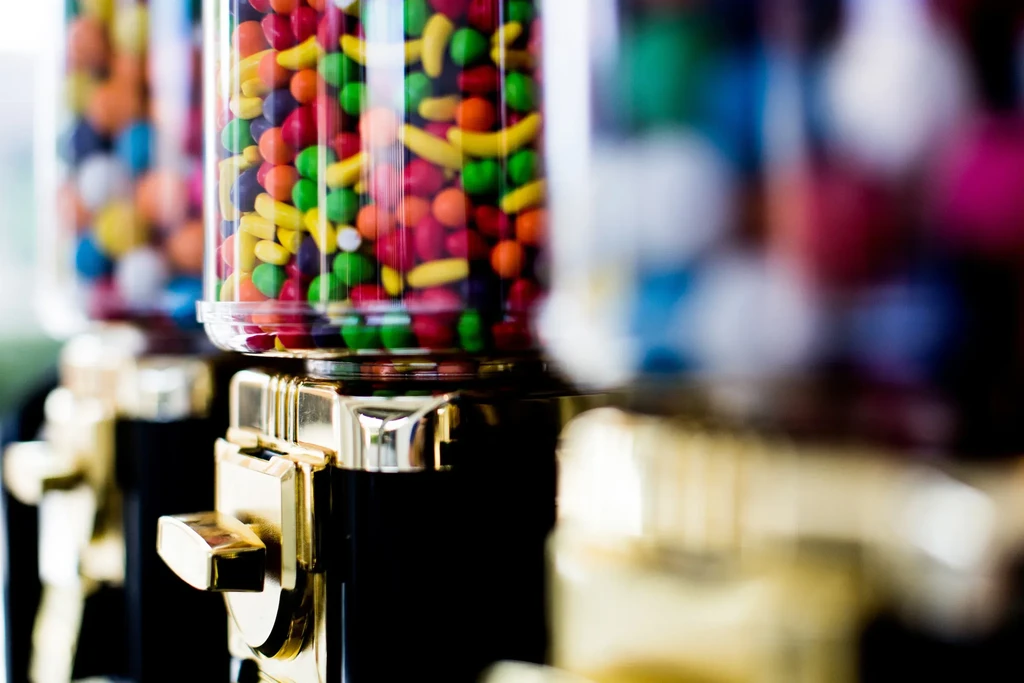 Colorful round and banana candies fill a golden-toned dispenser.