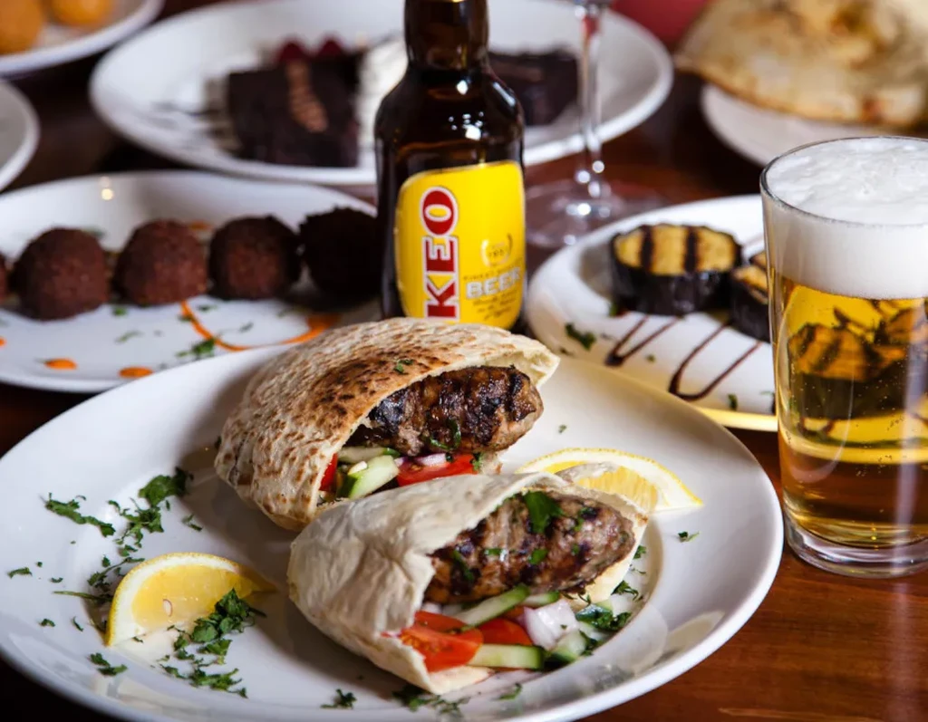 Grilled meat pita wraps, beer glass, and KEO bottle on table.