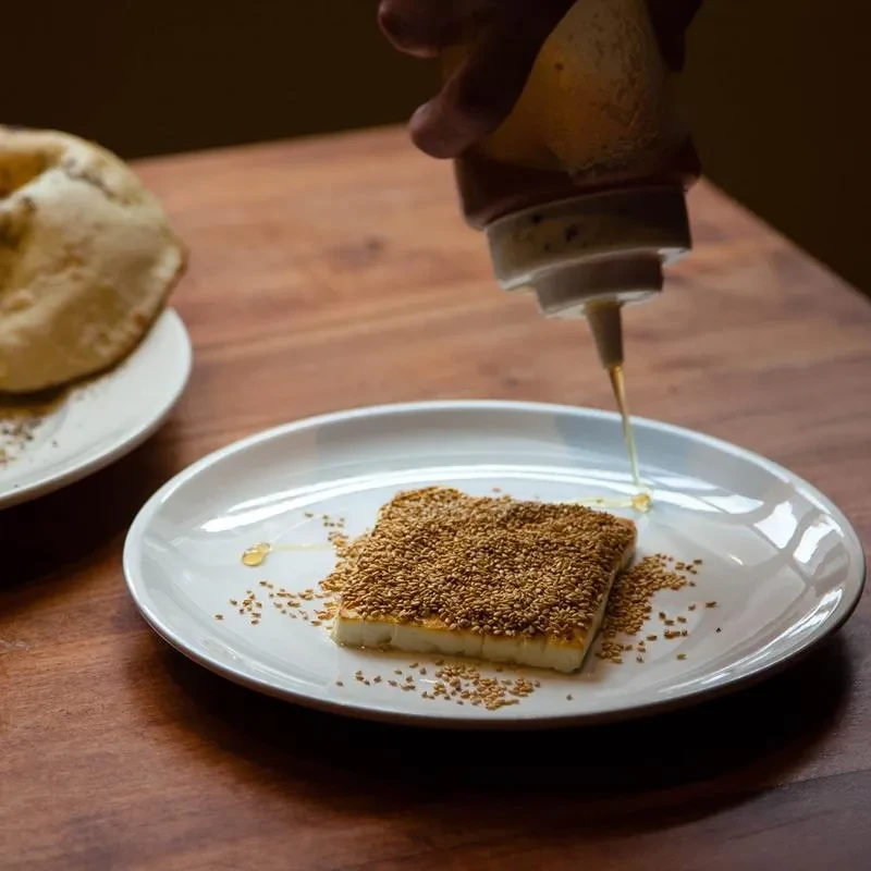 Hand drizzling honey onto sesame-crusted grilled cheese on a plate.
