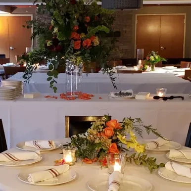 Dinner tables with white linens, candles, and orange-yellow floral centerpieces.