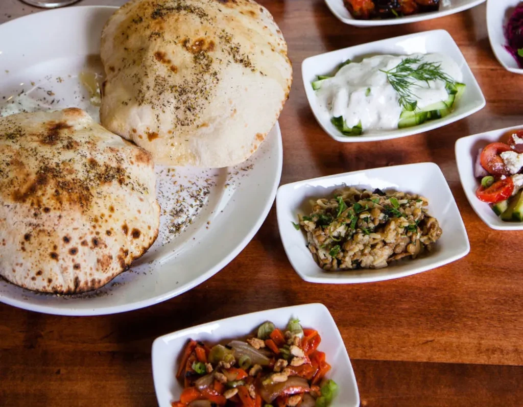 Mezze spread with bread, salads, and vegetables on a wooden table.